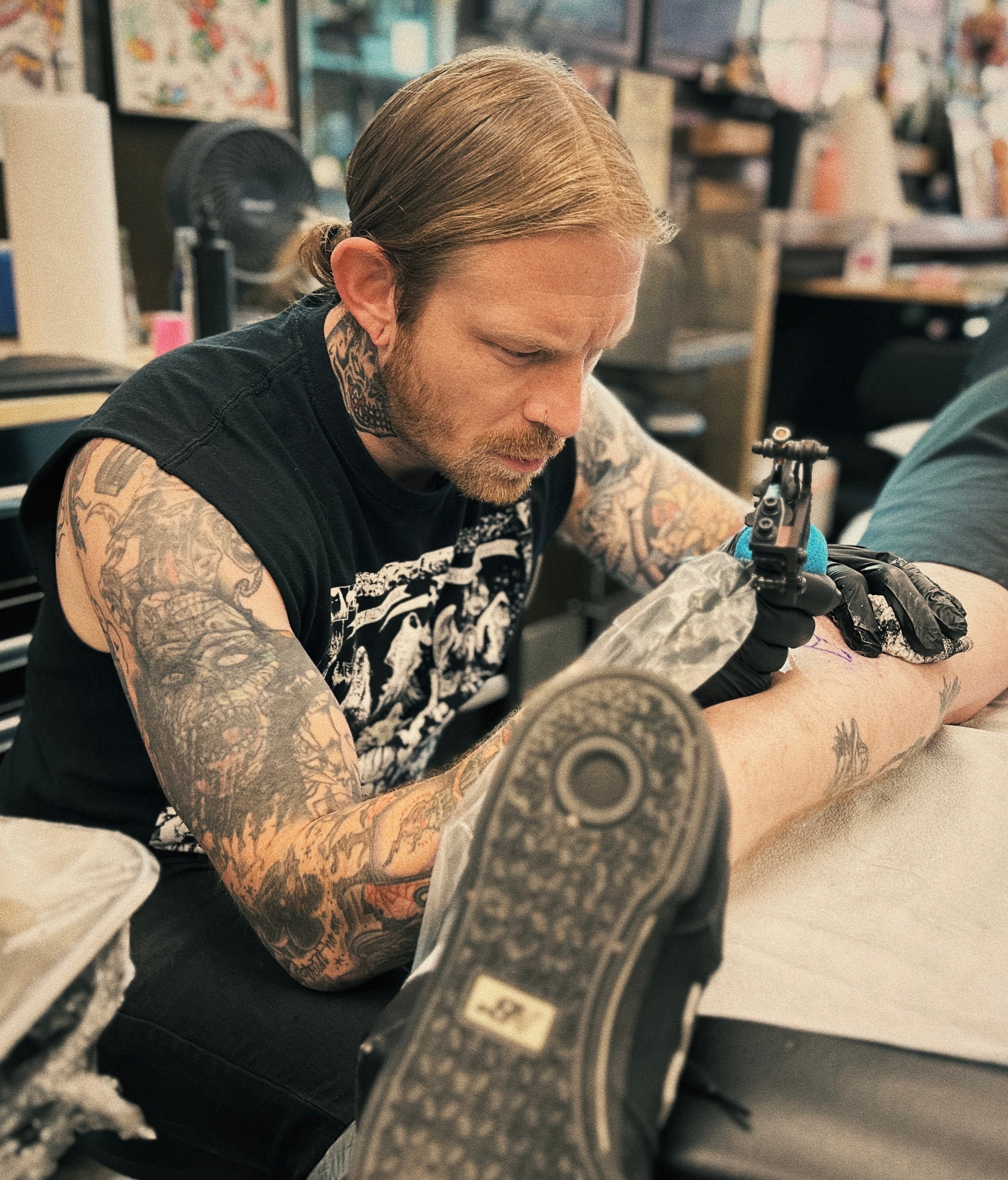An artist tattooing at Denver City Tattoo Club, flash sheets on the walls